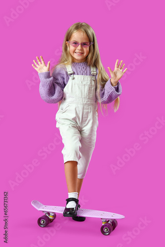 Cute little girl with skateboard on purple background