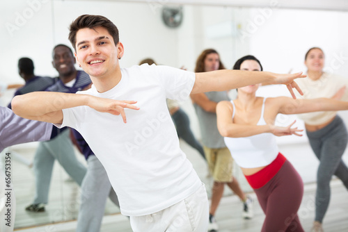 Smiling dark-haired young guy attending group choreography class, learning modern dynamic dances. Concept of active lifestyle ..