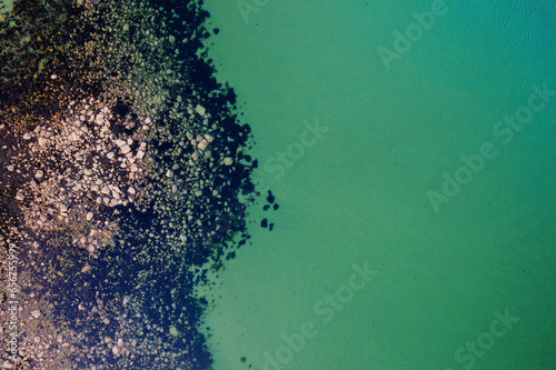 Aerial top down view on rough stone coast with green color water. Nobody. Nature shapes and forms.
