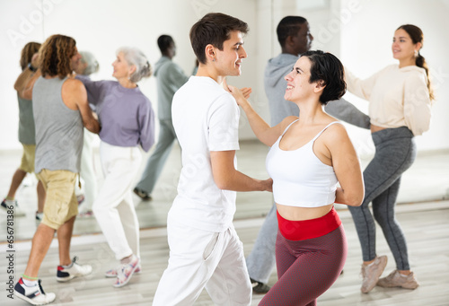 Cheerful young Hispanic woman and guy enjoying active dancing in pair during group training in dance studio