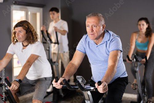 Portrait of elderly man taking indoor cycling class at fitness center, doing cardio riding bike