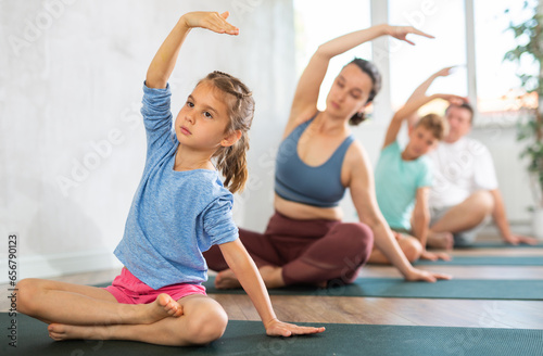 Little girl with parents and brother doing yoga in fitness class