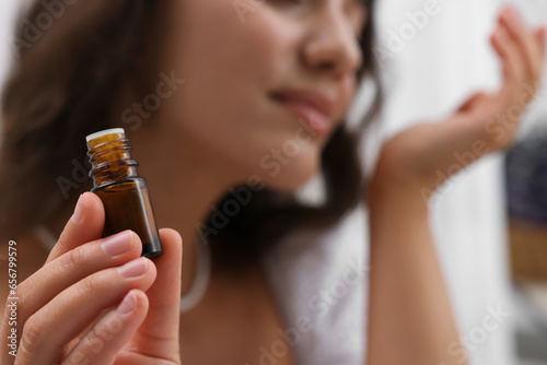 Woman with bottle of essential oil on blurred background, selective focus