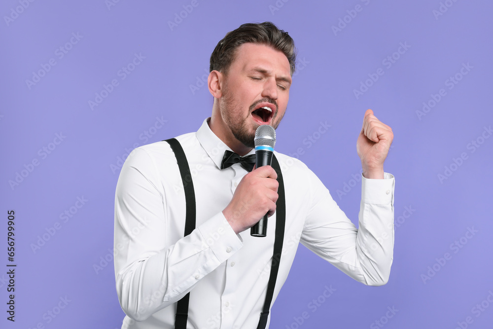 Handsome man with microphone singing on violet background