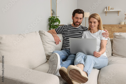 Happy couple with laptop on sofa at home. Space for text