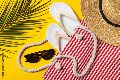 Flat lay composition with bag, palm leaf and other beach accessories on yellow background