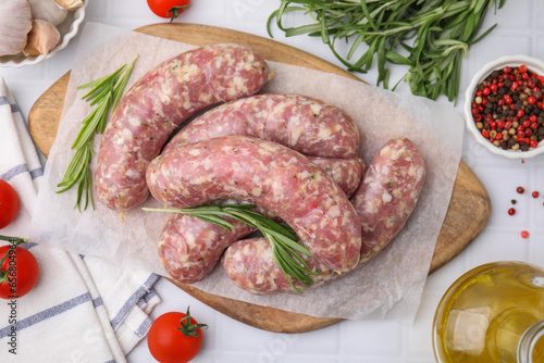 Raw homemade sausages and different products on white tiled table, flat lay