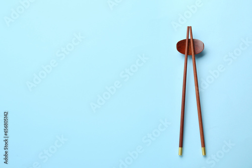 Pair of wooden chopsticks and rest on light blue background, top view. Space for text