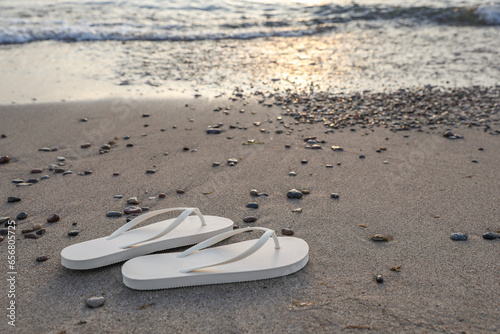 Stylish white flip flops on sand near sea. Space for text