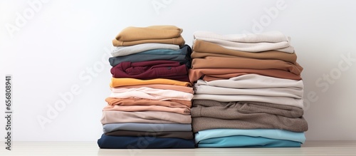 Neatly folded clothes stack assorted colored shirts sweaters and pants on table with white wall background Close up copy space studio image