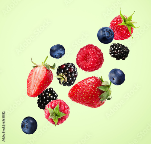 Many different fresh berries falling on pale green background