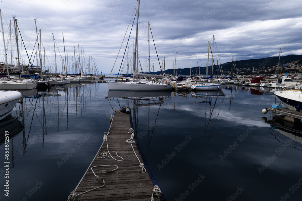 A harbour with sailing ships on the pier in Trieste, Italy. Yachts, schooners, masts at sunset. The cloudy sky is reflected in the calm water. A feeling of calm and serenity. 
