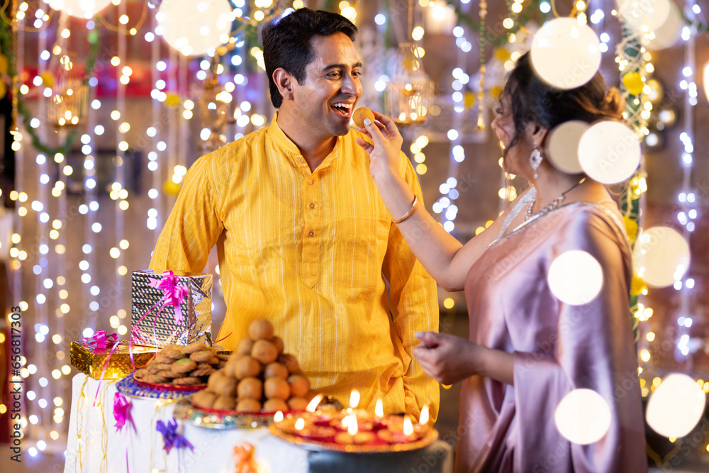 Obraz premium Indian smart couple eating sweet laddu on Diwali, selective focus