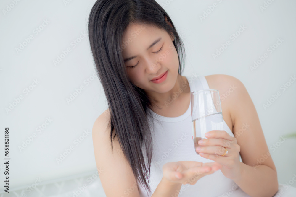 Beautiful young asian woman holding drug and glass of water while ill sitting on bed in the bedroom at home, female fever and healthcare while uncomfortable and unhappy, medical and lifestyle concept. Beautiful young asian woman holding drug and glass of water while ill sitting on bed in the bedroom at home, female fever and healthcare while uncomfortable and unhappy, medical and lifestyle concept.