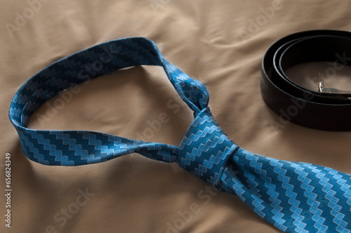 blue silk tie with a half windsor knot on a bed with a brown sheet and a dress belt as part of the men's attire pratt knot photo