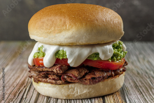 Churrasco italian sandwich popular in chile, round bread, beef, tomato and palta, mayonnaise, on wooden table. Typical Chilean food concept