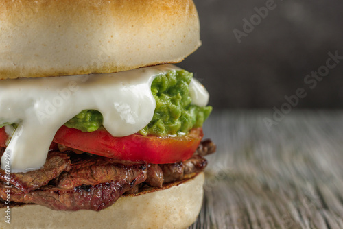 Churrasco italian sandwich popular in chile, round bread, beef, tomato and palta, mayonnaise, on wooden table. copy space. Typical Chilean food concept