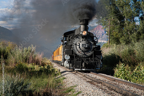a steam engine train with smoke billowing from the smoke stack travels through the Colorado mountains an autumn day