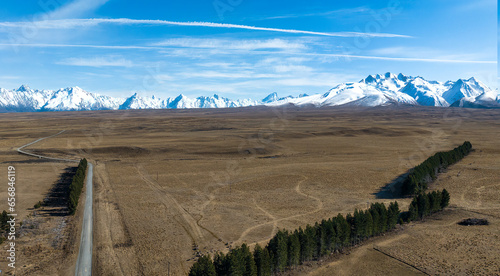 Long winding narrow gravel road across rural agricultural countryside towards the snow capped Southern alps mountain range