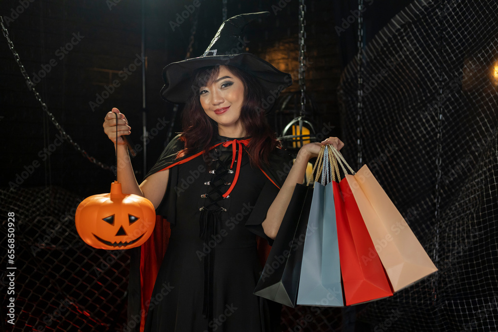 Asian girl in witch costume holding jack'o lantern for halloween party trick or treat concept with dark black background