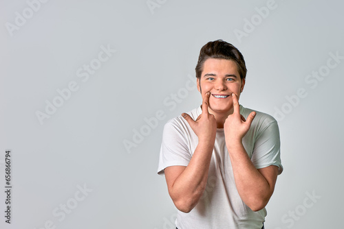 A man on a gray background shows a smile with his fingers