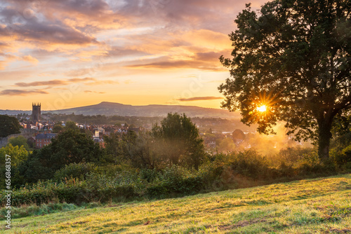 Colourful sunrise over the Shropshire town of Ludlow in the UK with a sun spear poking through the trees.  Shows the Town in the mid ground and Titterstone Clee hill in the background photo