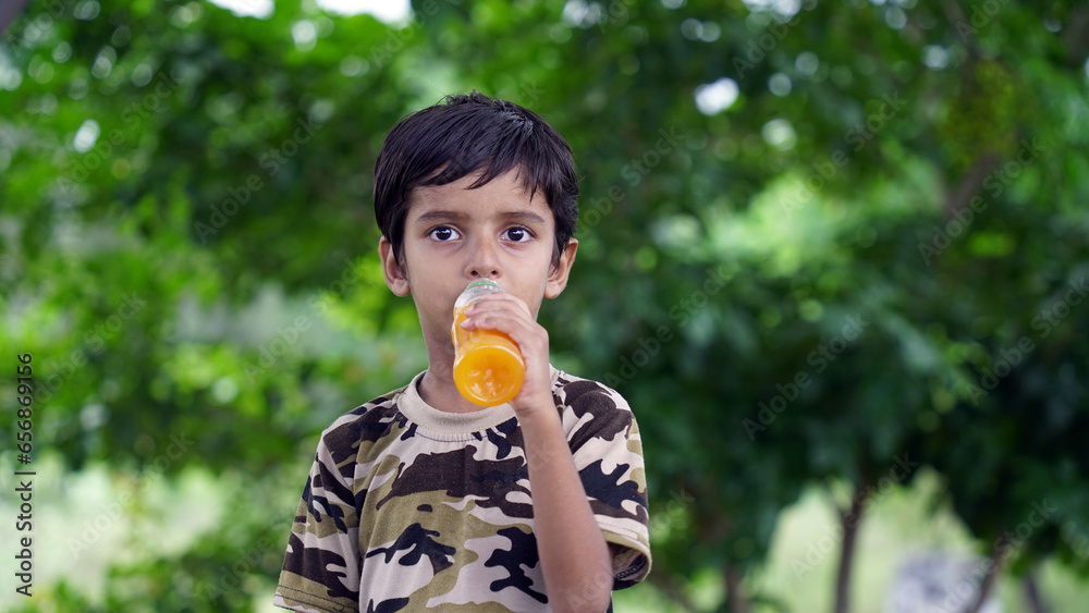 Fototapeta premium Happy Cute Indian boy drinking juice in the park, holding plastic bottle and showing thumb up. outdoor shot