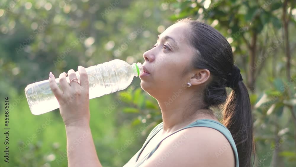 Latin woman drinking water from bottle during hiking in the park tree lined footpath. Medium shot. Travel concept. Latin woman drinking water from bottle during hiking in the park tree lined footpath. Medium shot. Travel concept.