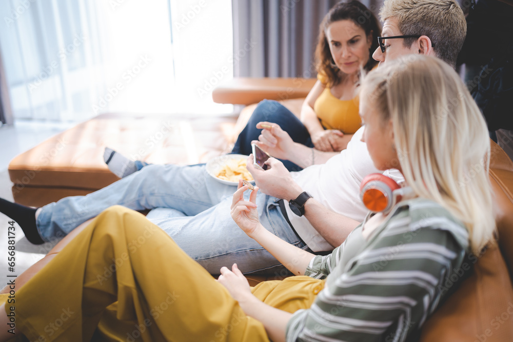Happy young family enjoy lunch together at home using mobile phone. Addicted online social media cellphone people eating in living room and watching display having fun. Concept of addiction smartphone