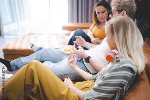 Happy young family enjoy lunch together at home using mobile phone. Addicted online social media cellphone people eating in living room and watching display having fun. Concept of addiction smartphone