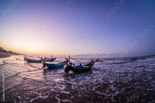 Silhouettes of fishermen on the beach pushing wooden boats out to sea to fish wooden boats on Ho Coc Vung Tau beach