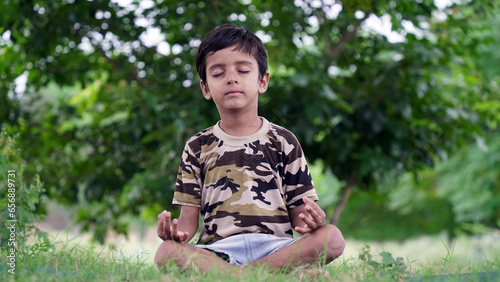 Little Indian boy practicing yoga in home garden. kid doing gymnastic exercises or meditating, health concept © Govind