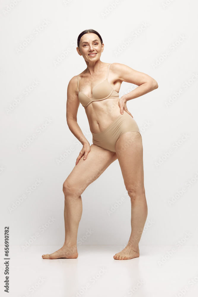 Full-length portrait of beautiful senior woman with well-kept healthy skin and body posing in underwear against grey studio background. Concept of age, natural beauty. body and skin care, health Full-length portrait of beautiful senior woman with well-kept healthy skin and body posing in underwear against grey studio background. Concept of age, natural beauty. body and skin care, health