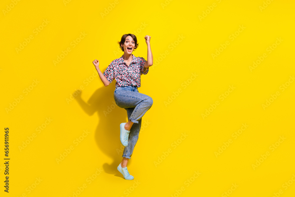 Full size portrait of overjoyed cheerful girl raise fists shout yes hooray empty space isolated on yellow color background