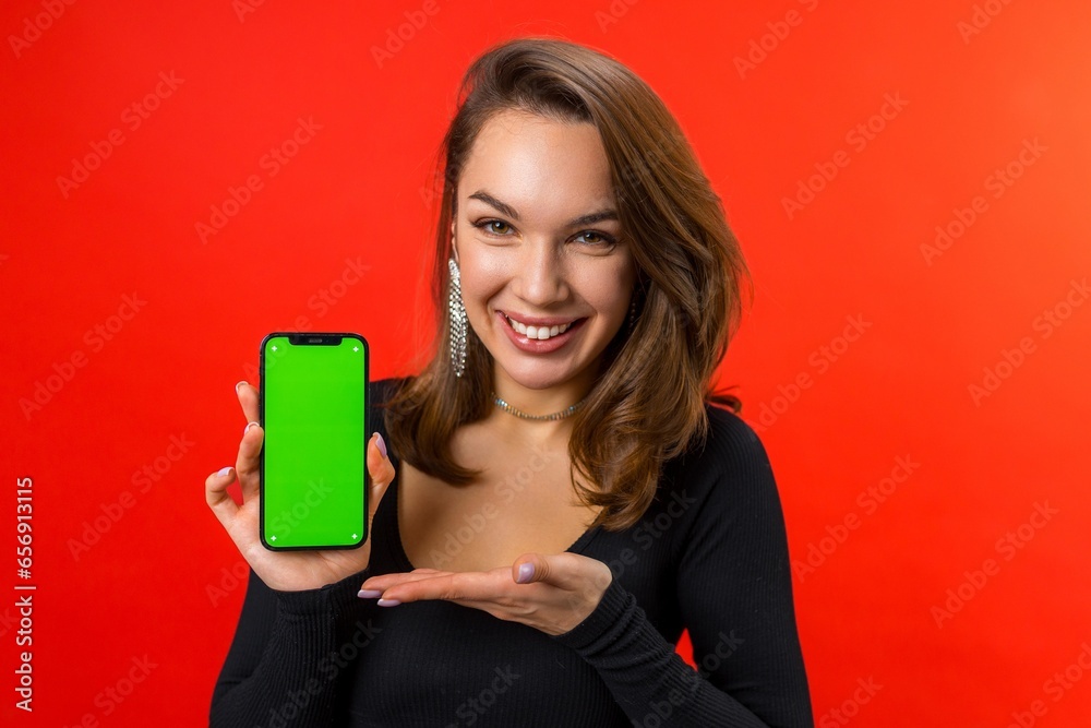 young energetic brunette lady dressed in a black blouse shows the screen of the phone on a red festive background young energetic brunette lady dressed in a black blouse shows the screen of the phone on a red festive background