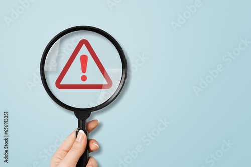 Hand-holding classic magnifier glass with triangle warning sign