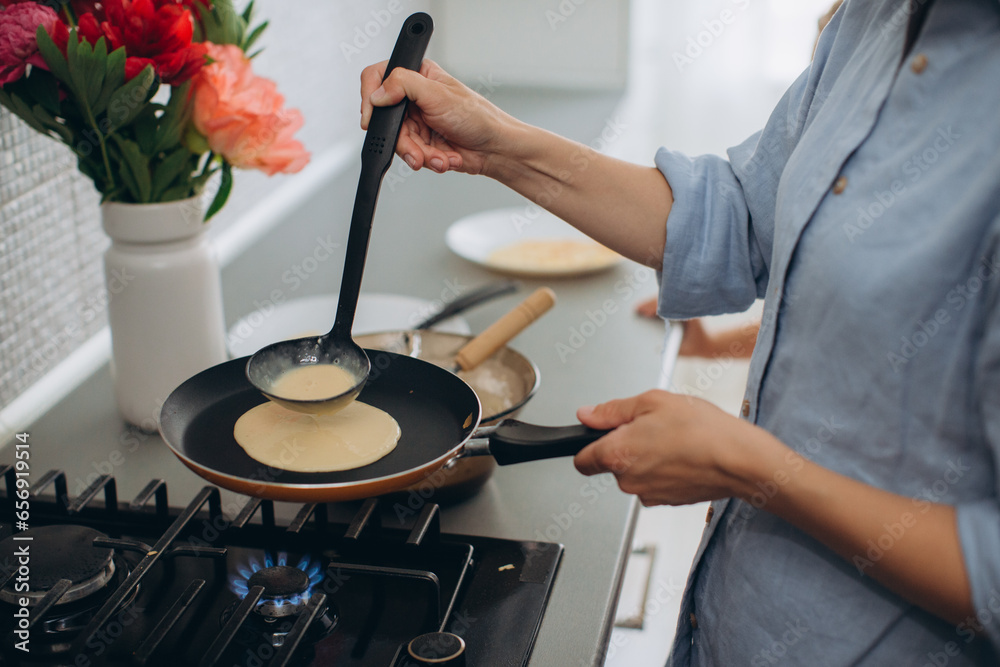 A young mother and her little daughter cook pancakes together for breakfast. Mother teaches daughter to cook. - obrazy, fototapety, plakaty 
