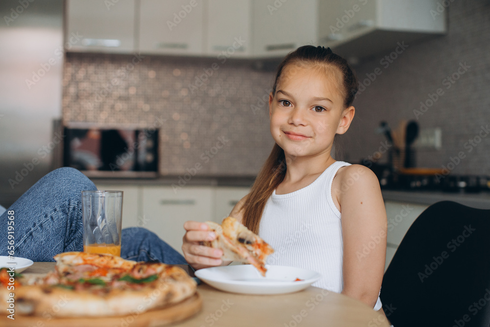 Mom and daughter are eating delicious pizza in the kitchen.