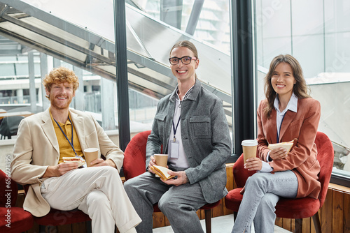 Foto three cheerful colleagues looking at camera and enjoying sandwiches and coffee,