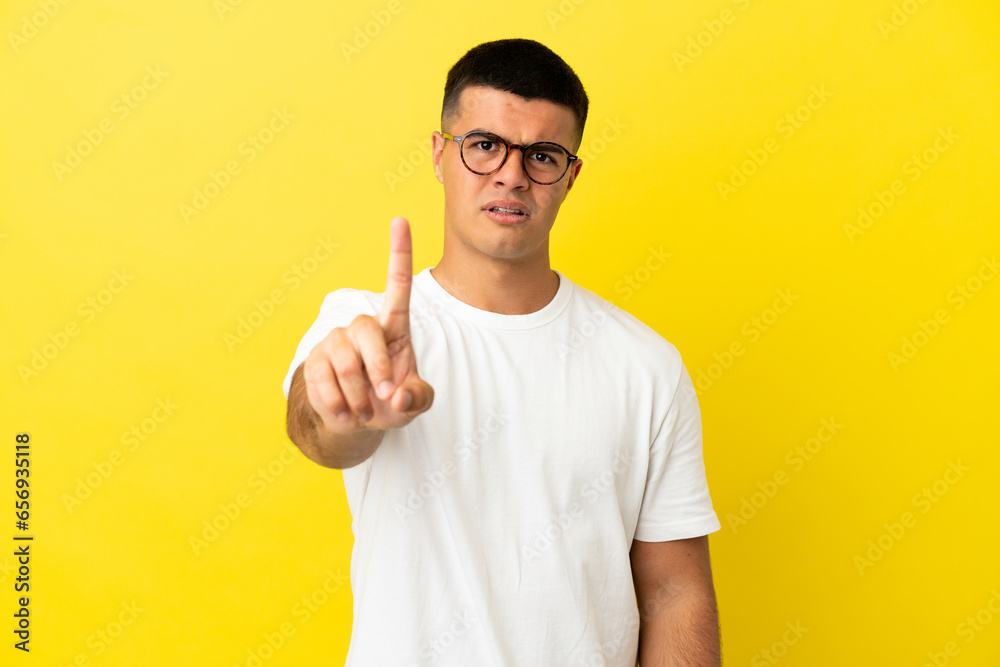 Young handsome man over isolated yellow background counting one with serious expression Young handsome man over isolated yellow background counting one with serious expression