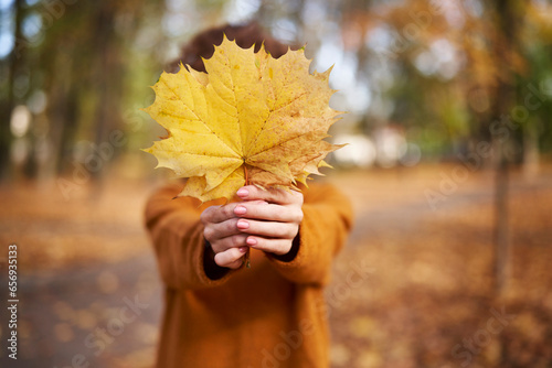 Woman holding maple leaf in front of face at autumn park photo