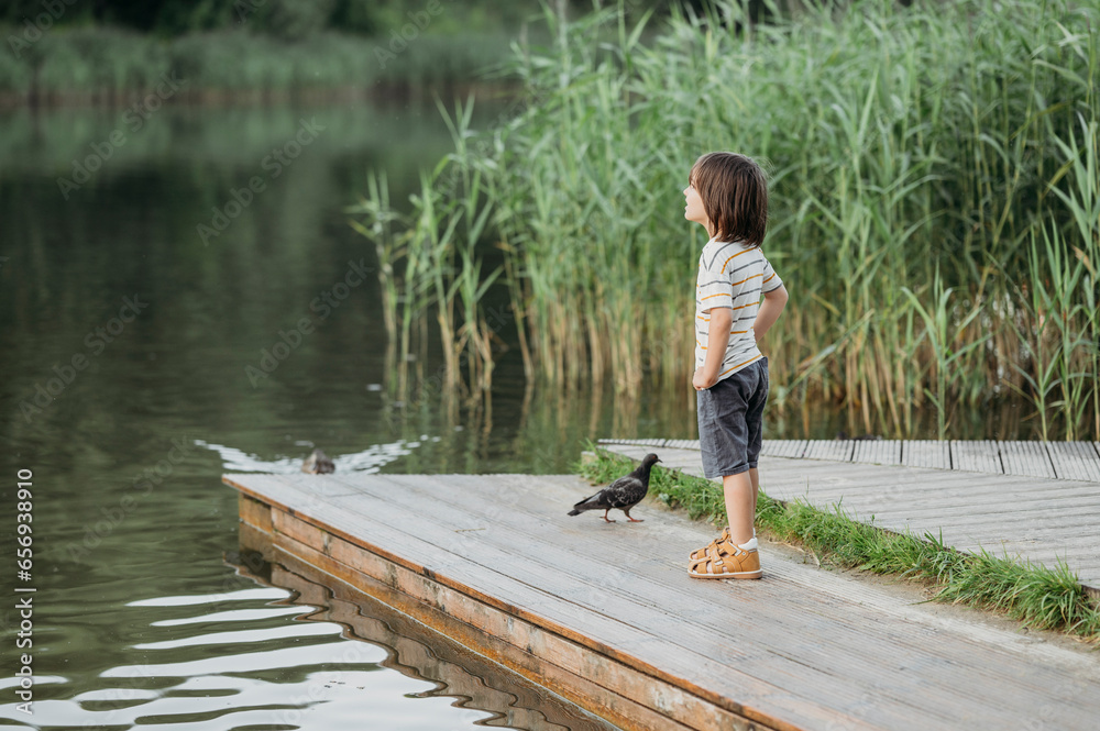Boy standing with pigeon on pier near lake Boy standing with pigeon on pier near lake