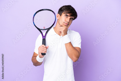 Handsome young tennis player man isolated on ocher background having doubts © luismolinero
