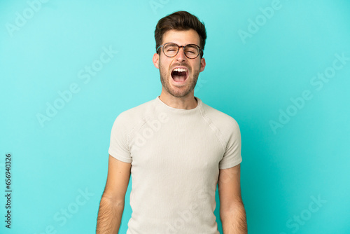Young caucasian handsome man isolated on blue background shouting to the front with mouth wide open