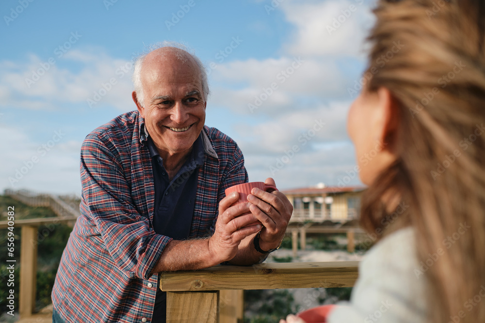 Happy senior man holding coffee cup and looking at woman on sunny day Happy senior man holding coffee cup and looking at woman on sunny day