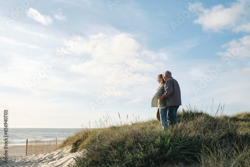 Senior couple standing together amidst plants at beach on sunny day photo