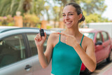 Young pretty woman holding car keys at outdoors and pointing it
