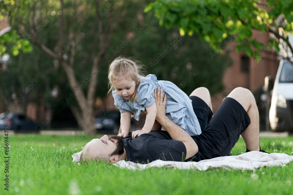 young father and his little daughter laying on the grass, kid is raised in the air young father and his little daughter laying on the grass, kid is raised in the air
