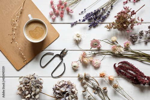 Cup of coffee, scissors and different kinds of dried flowers lying on white painted wood photo