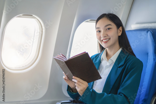 Female asian woman holding book while sitting in airplane  looking to camera.